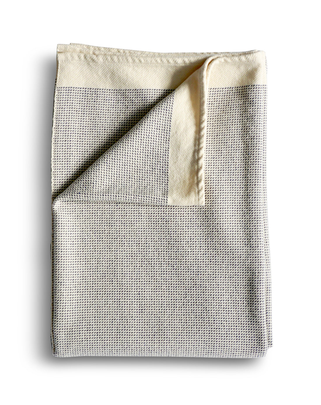 On a white background the combed cotton throw in Denim Dots is folded. The throw is a soft lightweight off-white color with a blue dotted pattern. Made of soft, natural cotton.