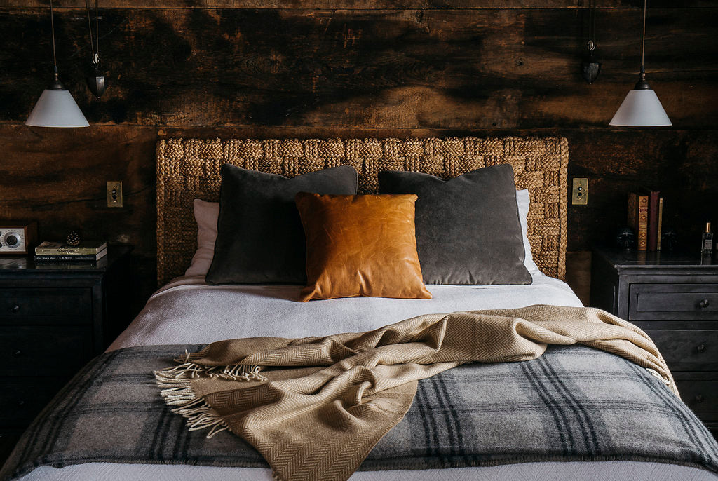 Evangeline's bright white herringbone woven cotton bed blanket on a made bed. Bed includes a wool bed blanket and throw from evangeline's collection, as well as decorative velvet and leather pillows. The headboard is a thick woven natural rope design, complementing the weave of the herringbone blanket.