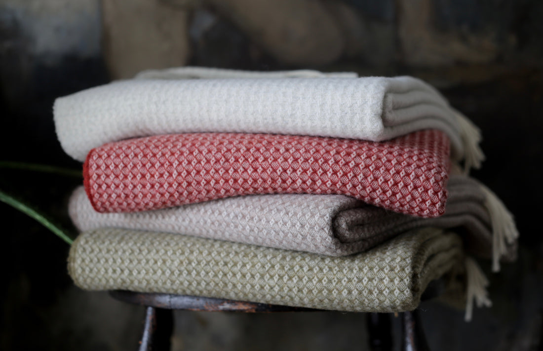 A stack of folded Evangeline Diamond throw with cashmere. Throws are Merino Lambswool and Cashmere, woven in Italy. Four muted sophisticated colorways cream on top, then clay red, taupe mushroom, olive green. Best throws in Maine. The perfect gift from Portland for housewarming or newlyweds.
