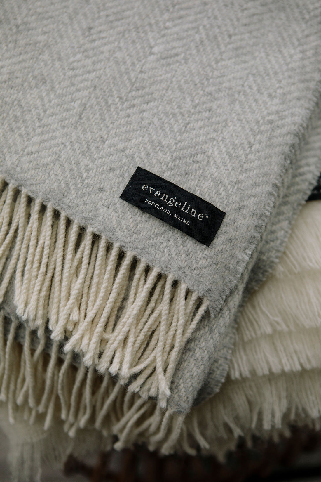 A detail photo of the cream fringe on the edge of Fog / light grey throw. Displays the sewn on evangeline Portland Maine tag on the bottom corner of the throw.