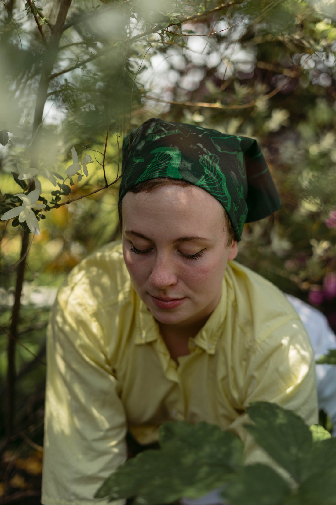 fair-skinned woman wears a green foraging evangeline bandana while gardening