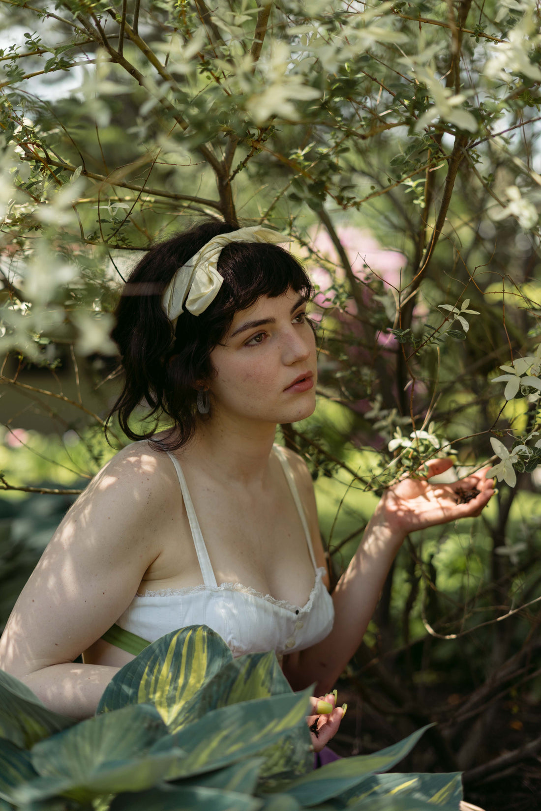 A fair-skinned woman with dark hair wears a cream and green bandana in the garden