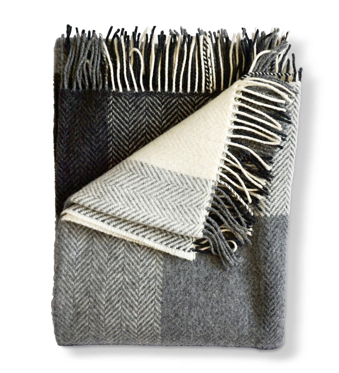 Folded Herringbone throw in Buffalo Check, a classic black and white colored throw with cream tassel detail. Timeless herringbone design. Super soft luster of cashmere. cozy comfort of merino wool. A chunky and cuddly classic. 95% Merino Lambswool and 5% Cashmere. Woven in Ireland.