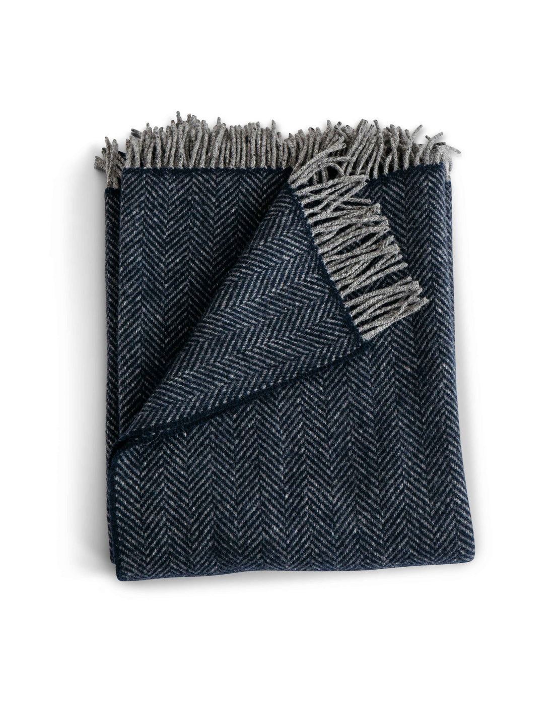 Folded Herringbone throw in Midnight a deep blue colored throw with grey fringe detail. Timeless herringbone design. Super soft luster of cashmere. cozy comfort of merino wool. A chunky and cuddly classic. 95% Merino Lambswool and 5% Cashmere. Woven in Ireland.