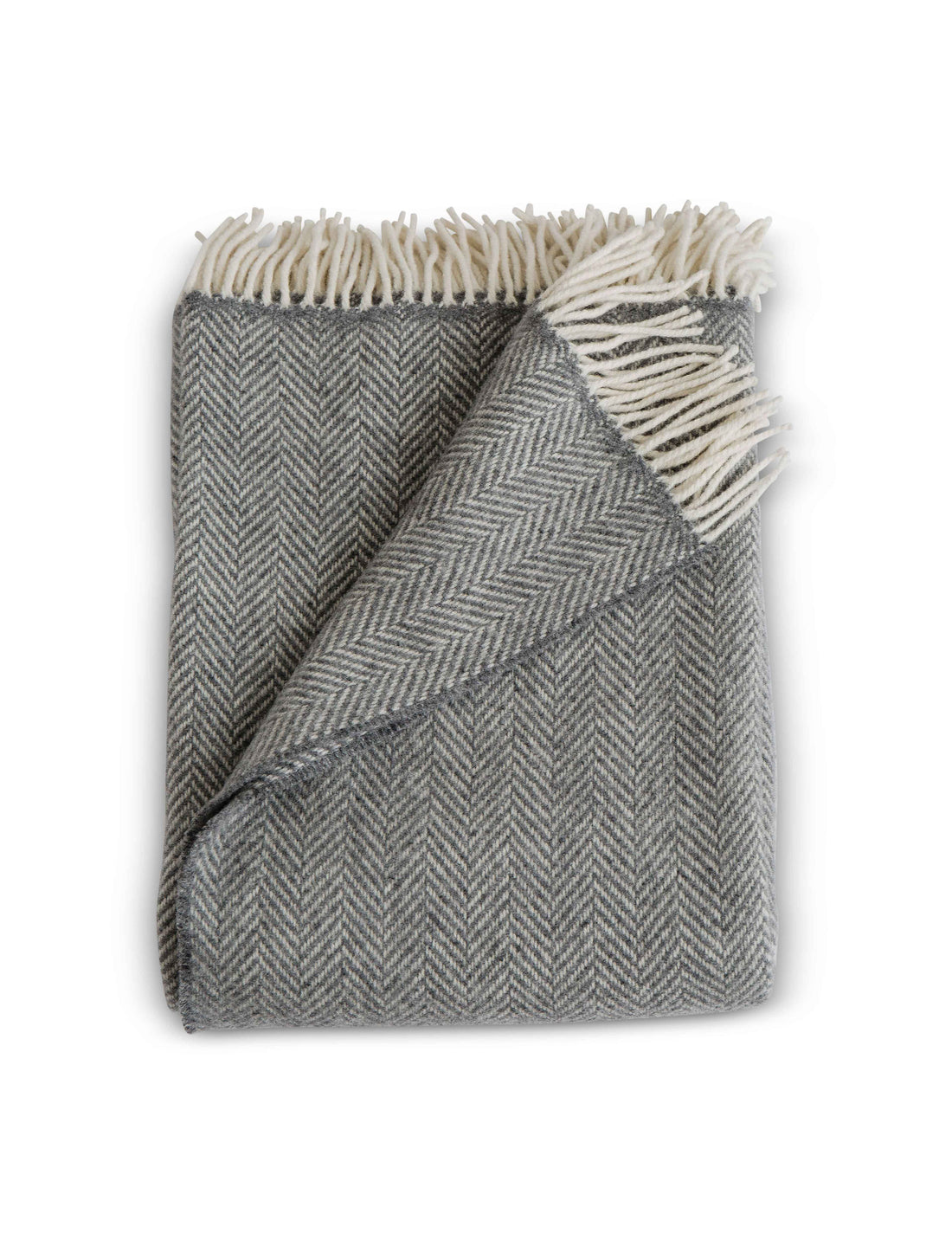 Folded Herringbone throw in Graphite, a medium dark grey colored throw with cream fringe detail. Timeless herringbone design. Super soft luster of cashmere. cozy comfort of merino wool. A chunky and cuddly classic. 95% Merino Lambswool and 5% Cashmere. Woven in Ireland.