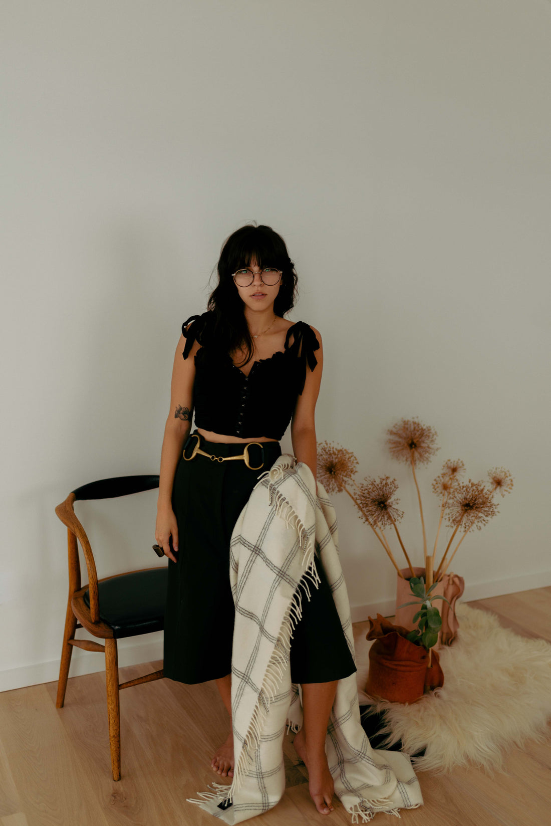 Elegant woman in black attire standing in a room, showcasing Evangeline Linens' luxurious 100% Merino wool throw blanket with a beautiful windowpane pattern.