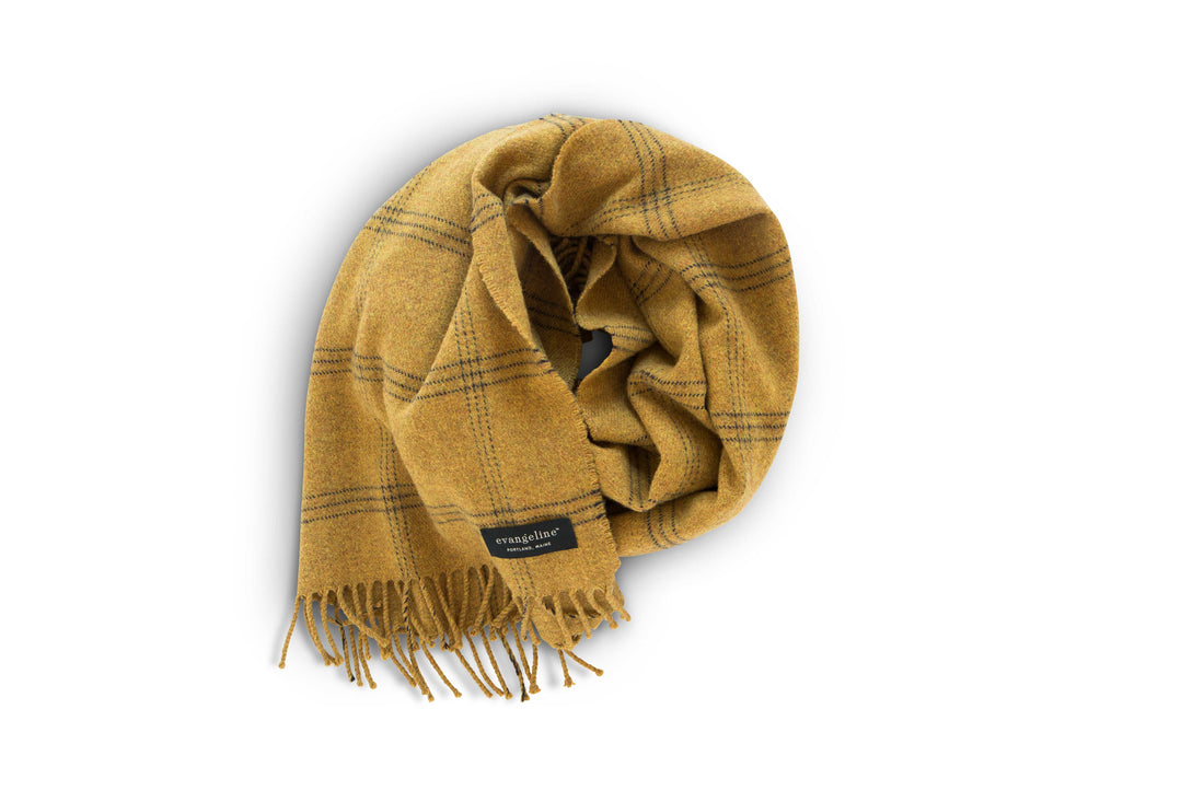 A sumptuous merino wool scarf, adorned with a striking yellow and black plaid pattern, elegantly drapes on a pristine white background.
