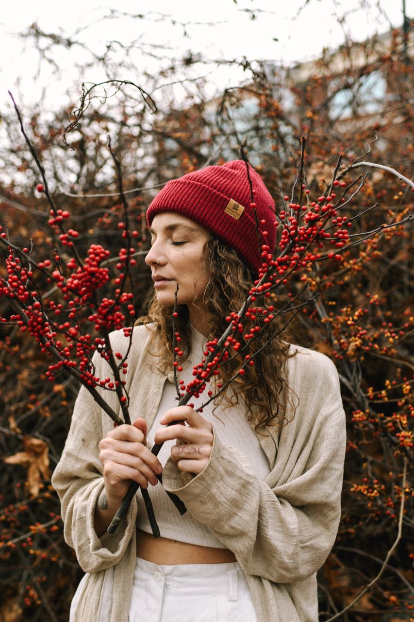 Fair skinned model wearing Evangeline Merino Wool Beanie Hat in color Scarlett - Red. The beanie hat has a small engraved leather tag on the folded up edge of the beanie that has the Evangeline Morel mushroom logo above 'Evangeline Portland Maine'.