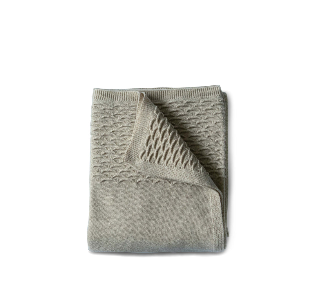 Evangeline Oatmeal Knit throw with Scalloped detail folded against white background.Super soft 'hand' of lambswool. Unique scallop texture. Has the energy of a treasured knit sweater.