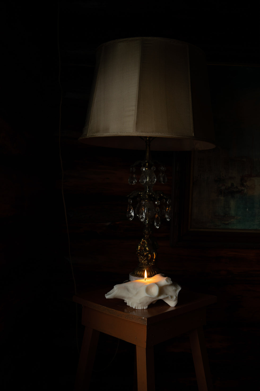 Hand-poured soy wax deer skull candle, lit on a side table, in a dark cabin.